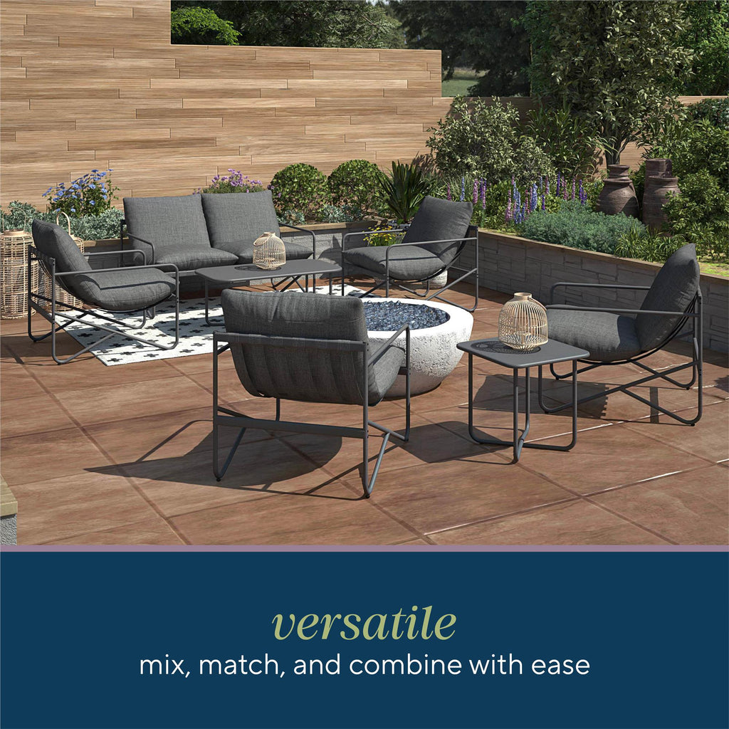 Introducing the Wrenn 4-Piece Sling and Cushion Conversation Set: a modern patio arrangement perfect for gatherings, featuring grey cushioned seating, a central fire pit, and side table with lantern surrounded by greenery and wooden paneling. Versatile: mix, match, and combine with ease.