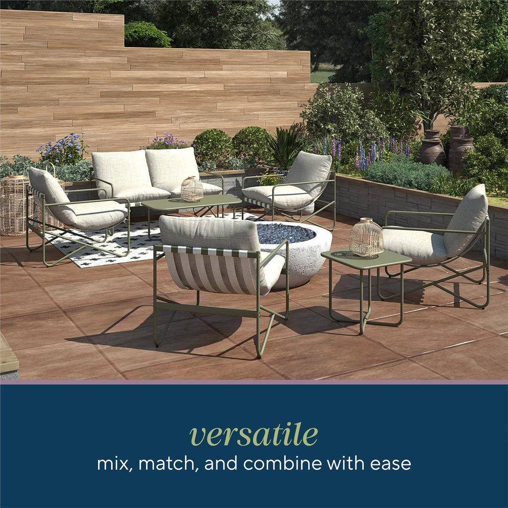 The outdoor patio boasts a modern setup with the Wrenn 3-Piece Sling and Cushion Set in Spanish Green. A sofa and round tables encircle a central fire pit, while a wooden fence and lush greenery provide an inviting backdrop. Versatile - mix, match, and combine with ease for any occasion.