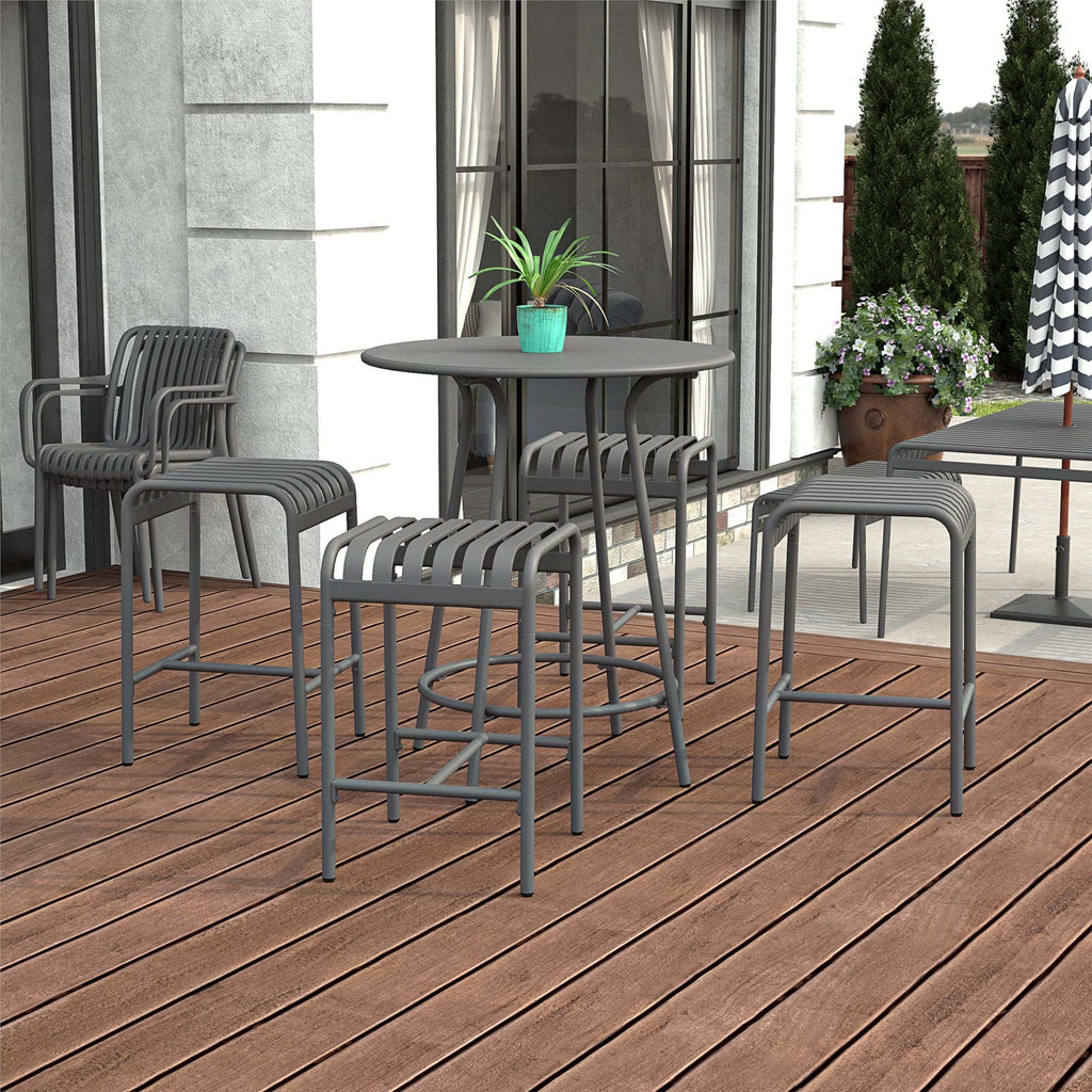 The Ola 5-Piece High Dining Set creates a modern outdoor patio with its tall, round table and surrounding high-quality steel metal chairs and stools with horizontal slats. A small plant sits atop, complemented by wooden deck flooring and building windows in the background.