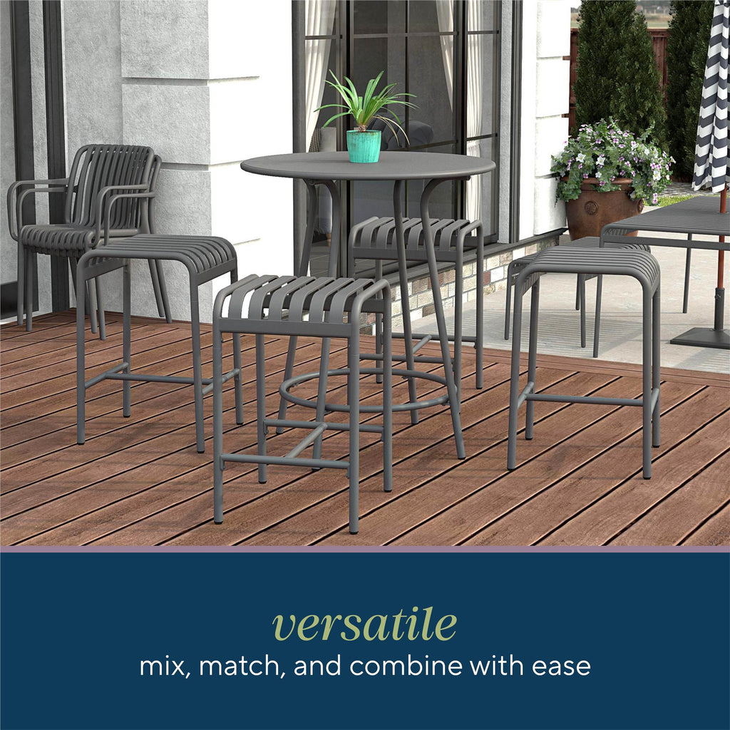 The Ola 5-Piece High Dining Set features a round table and four slatted metal bar stools, crafted from durable high-quality steel. Positioned on a wooden deck near white glass doors, its surrounded by greenery and complemented with a patio umbrella in the background.