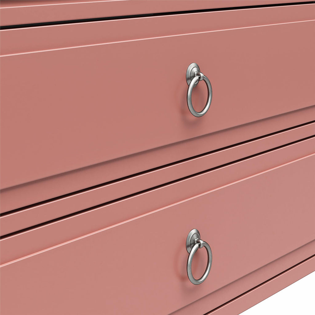 Close-up of a pink dresser styled as an elegant nightstand with two drawers. Each drawer features a silver ring handle at the center, enhancing its sleek, modern design. Reminiscent of the Her Majesty 2 Drawer Nightstand, its minimalist grooves add a refined touch.